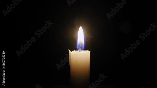 Single white candle burns with a gently flickering flame in the center of the frame. The isolated flame is the only source of light against a completely black background.