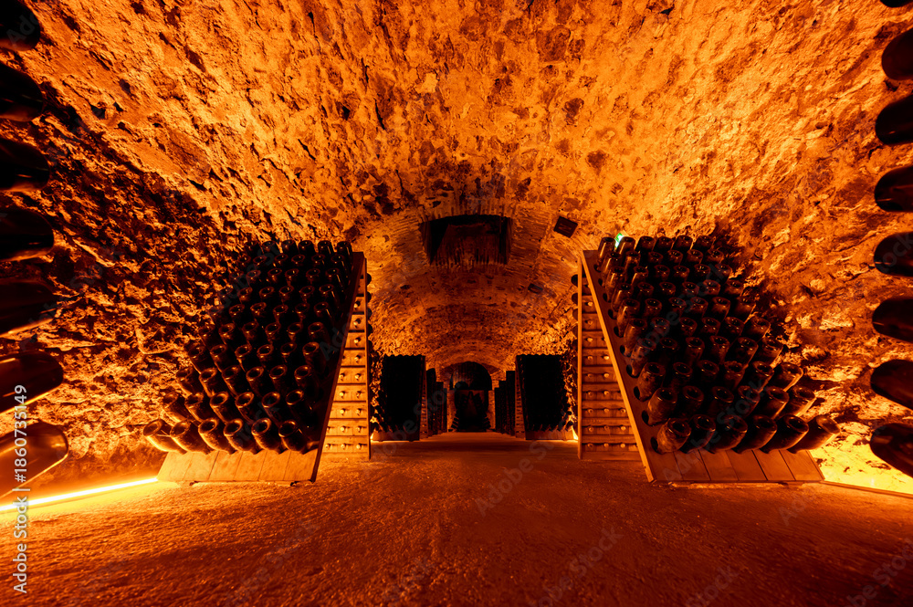 Fototapeta premium Riddling or remuage sediment to the bottle neckin deep underground caves on pupitre wooden racks, traditional method making champagne sparkling wine in Reims, Champagne, France