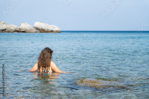 Firodi beach in Magganitis village of Ikaria island, Greece with young woman back behind swimming in water of Icarian sea