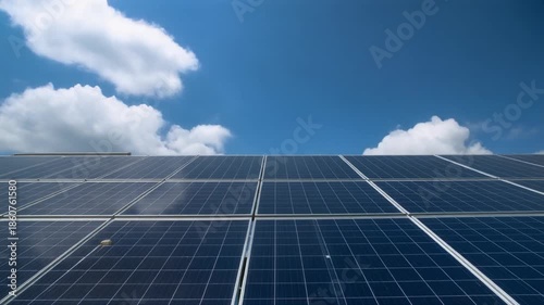 Close-up view of dark blue solar panels capturing sunlight under a bright blue sky with scattered white clouds, symbolizing renewable energy.