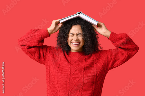 Young African-American woman with open book on her head on red background