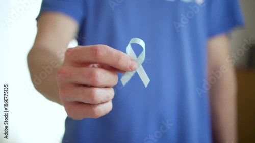 A man holds a blue satin ribbon in his hand, representing prostate cancer awareness, early detection, and support for patients and their families.