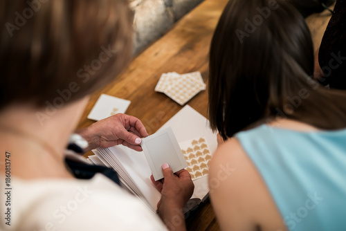 Tableau sur toile Wedding guests browsing instant photos in a handmade guest book, capturing candid memories at an intimate celebration with natural light, wooden table details, and elegant documentary wedding style