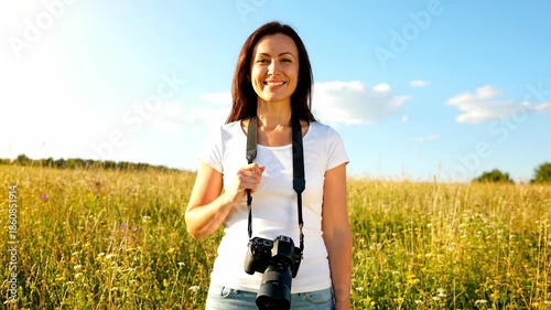 Happy woman photographer smiling in a sunny summer field with camera around her neck