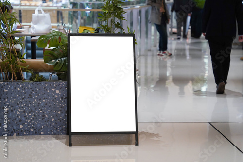 Blank white outdoor advertising stand sandwich board mock up template. Clear street signage board placed by an indoors dinning area of a restaurant in shopping mall.