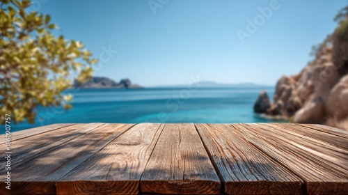 A wooden table stands on a shoreline. The blue water stretches out to distant hills under a clear sky. The sun shines brightly casting shadows on the table.