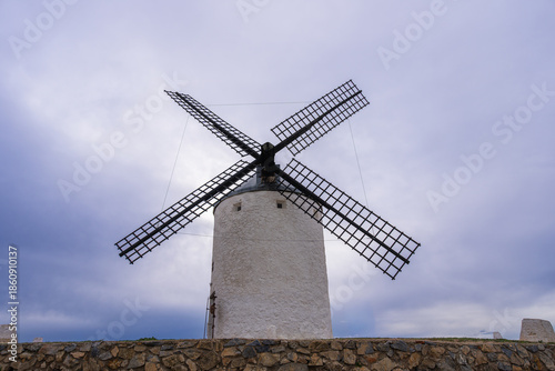 A traditional stone windmill stands on a grassy hill in Consuegra, Spain, famous as the site of Don Quixote battle in La Mancha.