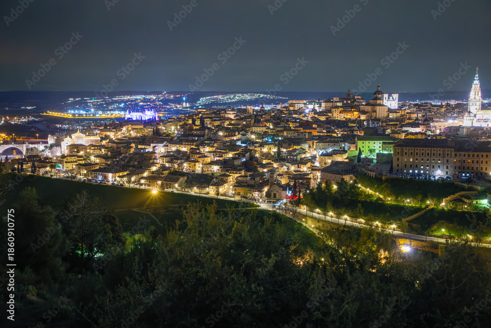 Fototapeta premium Stunning night cityscape of Toledo, Spain. The historic skyline and Rio Tajo river are illuminated under a dark sky at the Mirador del Valle.