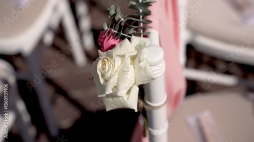 Flowers are arranged on chairs for a gathering in a garden. Guests are expected to arrive soon. The setting is bright and the decorations are simple and elegant.