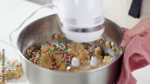 Homemade cookie dough with colorful sprinkles being mixed in a stainless steel bowl with a hand mixer.