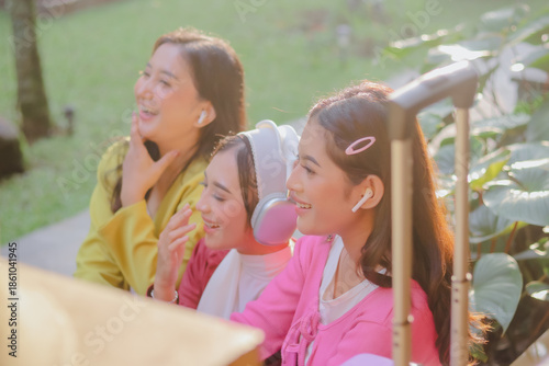 Three radiant young women are sharing a cheerful time together outdoors. They are happily laughing and engaging in conversation with youthful carefree energy in the sunshine.
