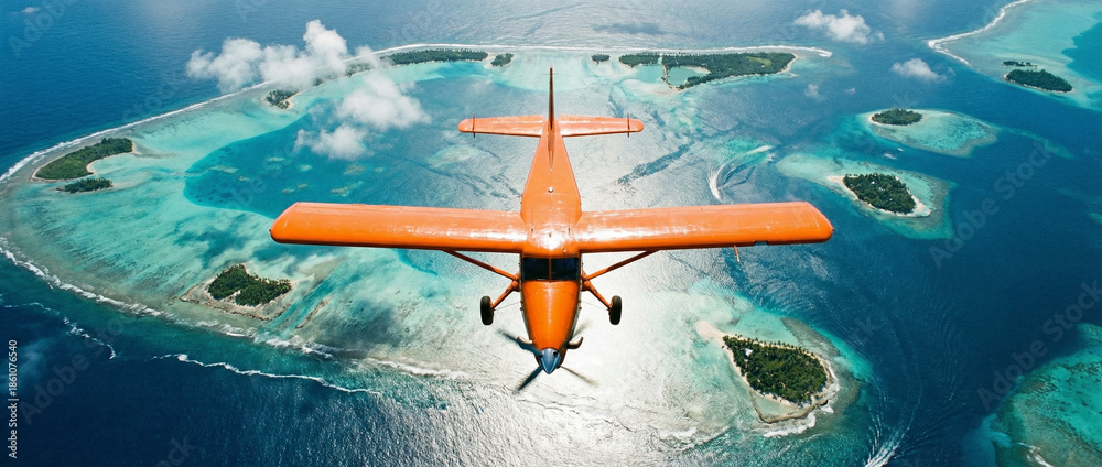 Naklejka premium Top-down aerial of an orange bush plane flying over tropical lagoons