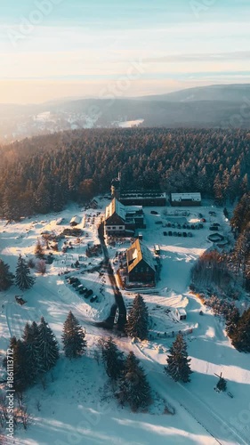 The clip shows a winter view from Kralovka lookout tower in the Jizera Mountains. Snow covers the ground and trees. The area features buildings and roads surrounded by forests.