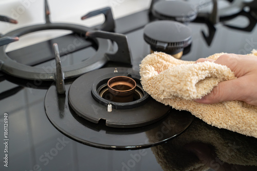 Hand wiping black gas stove burner with cloth during home spring cleaning