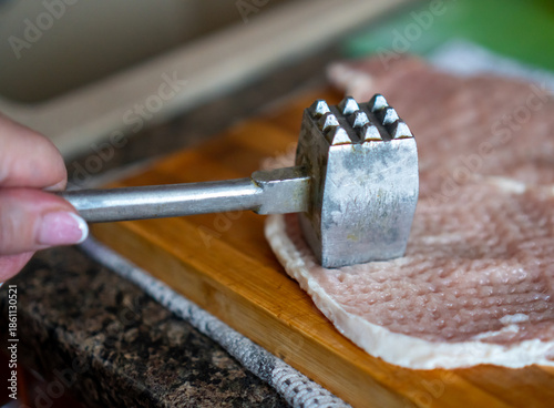 Fotografi A woman tenderizes fresh raw pork chops with a metal mallet on a wooden cutting board
