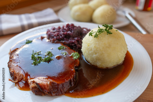 Delicious homemade roast pork with red cabbage, potato dumpling and gravy on a plate. Traditional german food