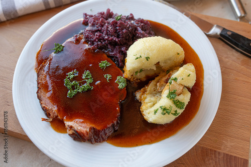 Delicious homemade roast pork with red cabbage, potato dumpling and gravy on a plate. Traditional german food