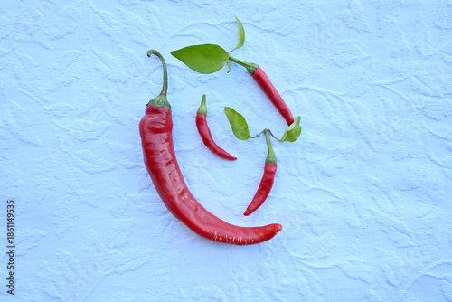 Organic red hot chili peppers with green leaves arranged on a blue fabric background. Minimalist culinary concept for healthy cooking.