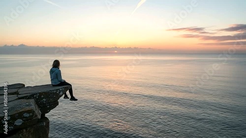 Person sitting on cliff during sunset over ocean