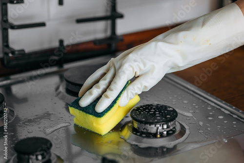 Photos Person wearing rubber gloves is cleaning a stainless steel gas stove with a spon