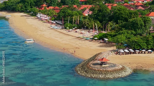 Aerial drone view orbiting a tropical beach resort in Sanur, Bali with clear water