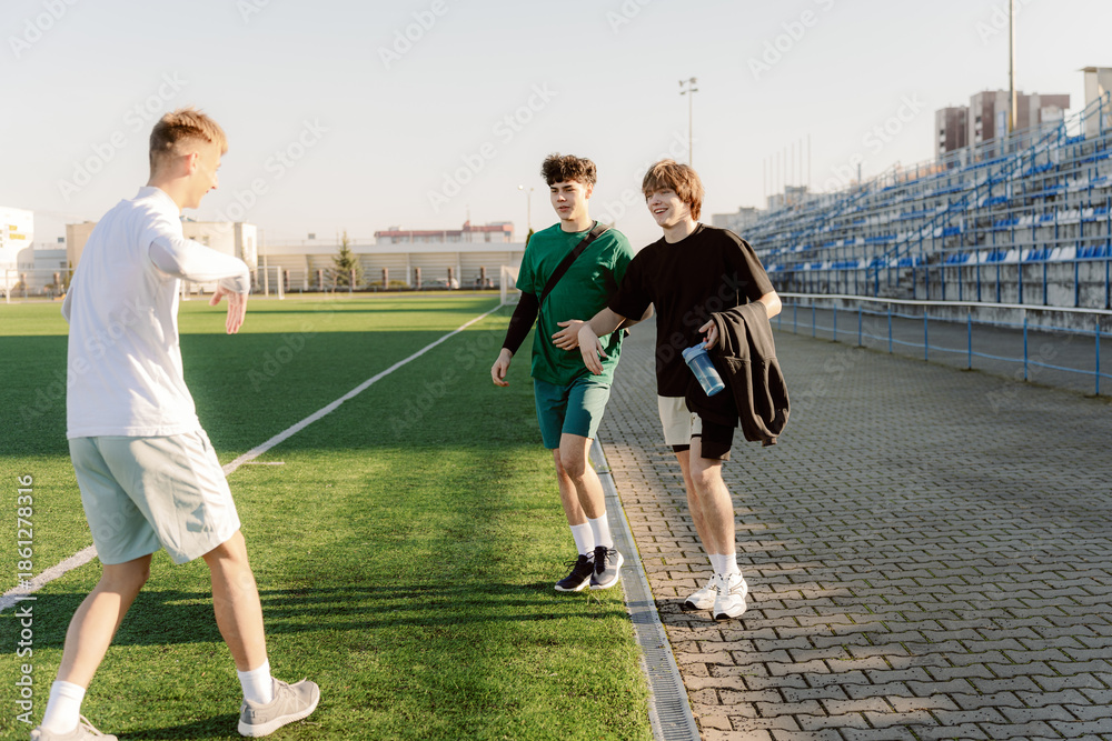 Obraz premium Three young friends walk together on a lush green sports field, enjoying the warm afternoon sun. Laughter fills the air as they discuss their practice session and share stories.