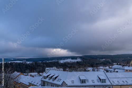 Snowy rooftops under a dramatic sky with clouds rolling in, capturing winter's quiet beauty in a serene landscape