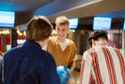 Laughter fills the air as three friends gather at the bowling alley. One holds a bright blue bowling ball, ready to take his turn while the others share smiles and banter.