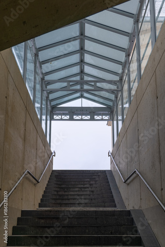 Sturdy stairs lead upward through a modern glass structure toward a cloudy sky