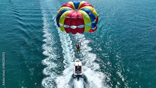 Aerial view of person parasailing behind a speedboat on a sunny day.