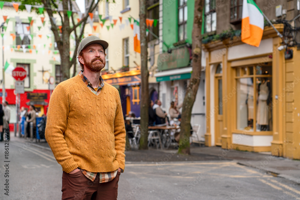 Fototapeta premium An Irish man in a yellow sweater stands in the heart of Galway's Latin Quarter on Quay Street, a vibrant pedestrian area famous for its colorful storefronts and lively atmosphere.