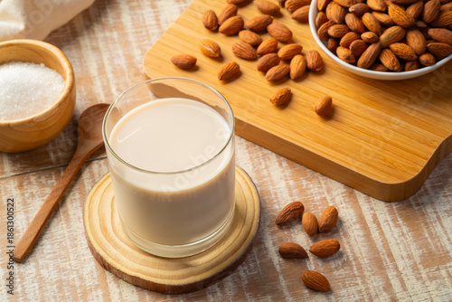 Almond milk in the glass with almond on wooden plate.