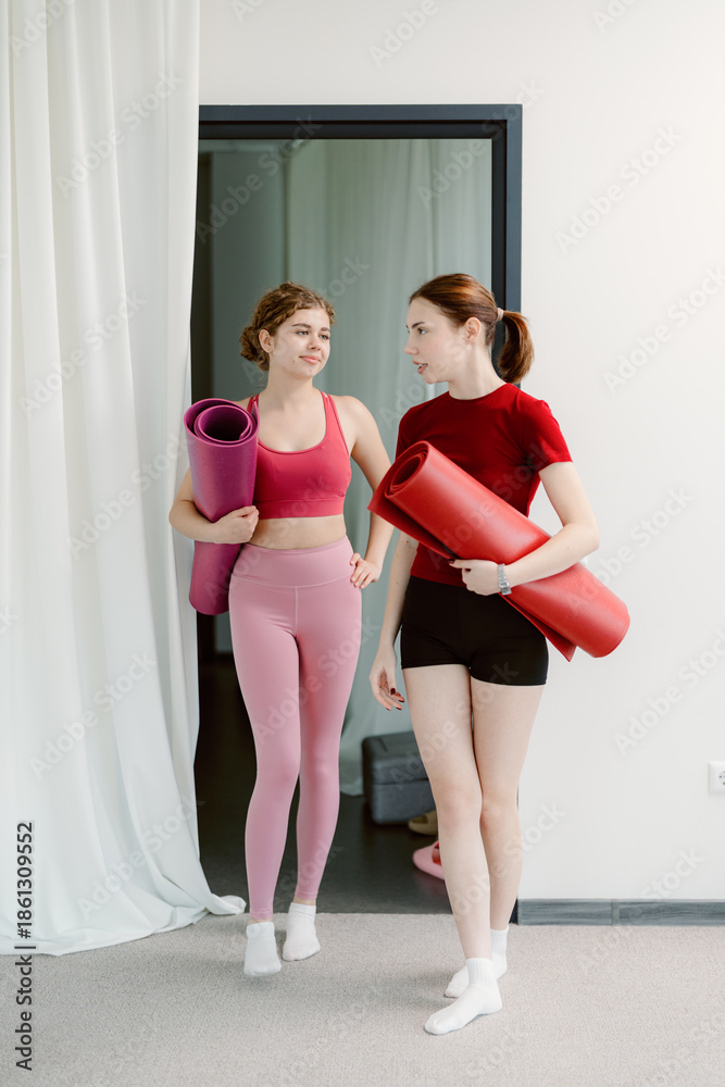 Obraz premium Two friends walk into a spacious yoga studio, each carrying a colorful yoga mat. They share smiles and excitement as they prepare for a rejuvenating session together.