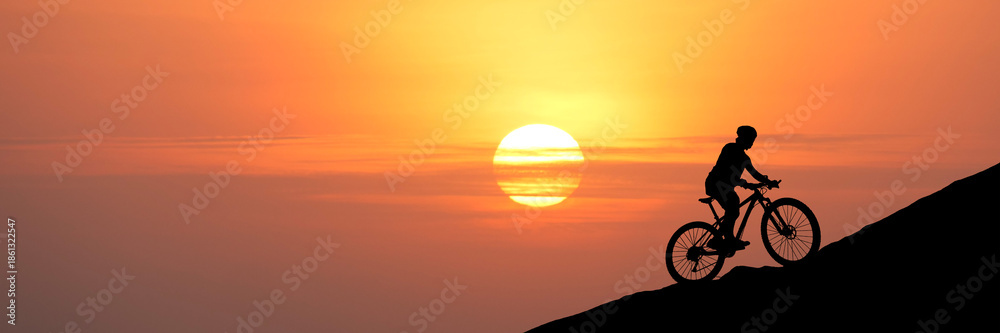 custom made wallpaper toronto digitalA silhouette of a cyclist riding uphill towards a vibrant sunset. The rider is pedaling against a backdrop of a warm, orange sky