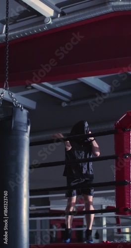 Vertical 4k footage of a male boxer is stretching his arms before training in a dark boxing gym. A focused male boxer stretches his arms in the dimly lit boxing gym before training.