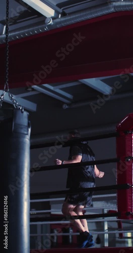 Against soft gym light, the boxer's silhouette flows effortlessly, combining strength and determination in a rhythmic jump rope session. Slow motion vertical 4K footage.