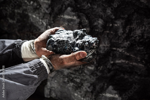 Fotografía Hands of coal miner holding coal or valuable minerals in the dark of the mine un