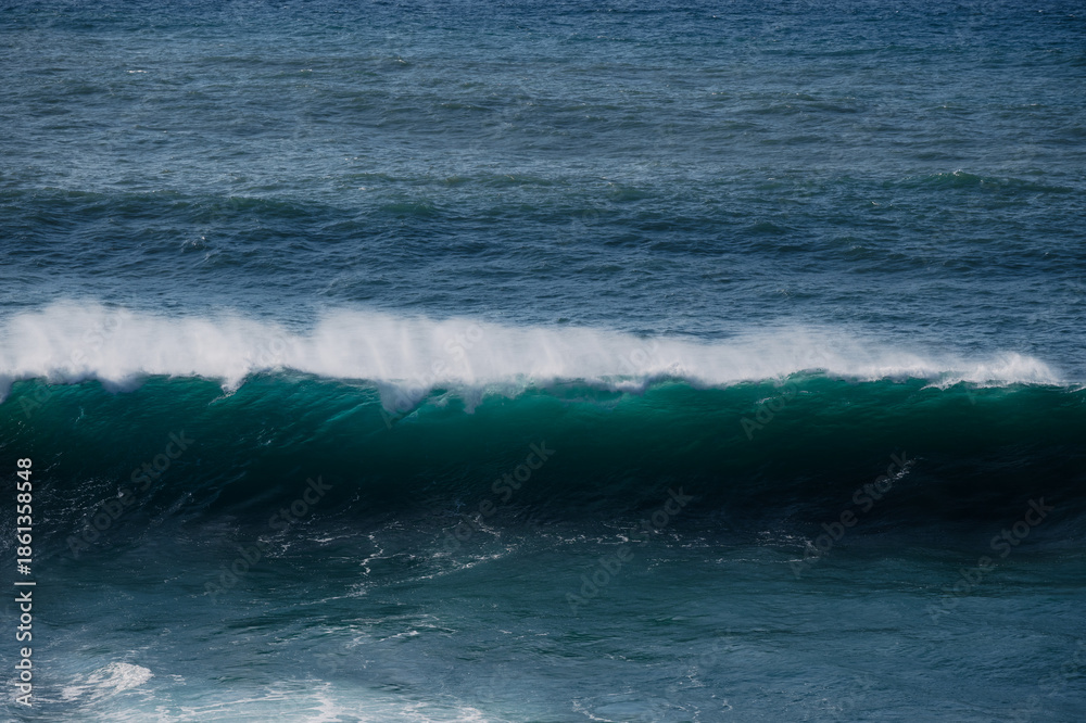 Fototapeta premium A powerful ocean wave rolls toward the shore with deep blue and green hues