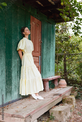Foto Woman in a pale yellow dress leaning against a green wooden wall outdoors, seren