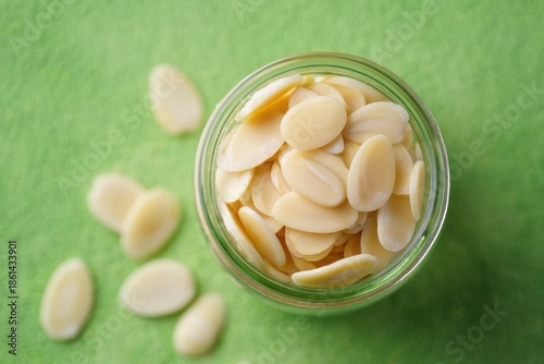Sliced almonds in a jar on a green textured background slivered almonds nuts