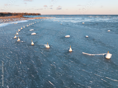 Aerial drone view of frozen coastline at Paljassaare peninsula in Tallinn, Estonia, with ice-covered navigation buoys at winter sunset.