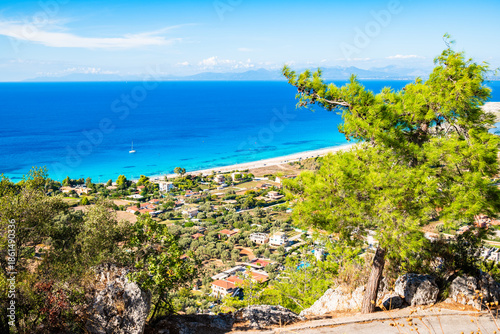 View of beautiful Agios Ioannis beach with green pine tree in foreground, Lefkada island, Greece
