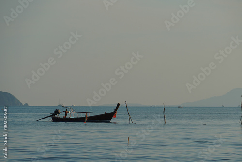A longtail boat is approaching the shore in the evening