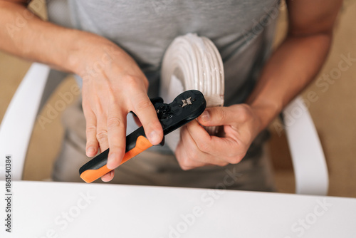 Картината върху платно Person hands holding cable crimping tool, preparing white electrical wire for secure connection, performing precise task of installation or repair and ensuring proper conductivity