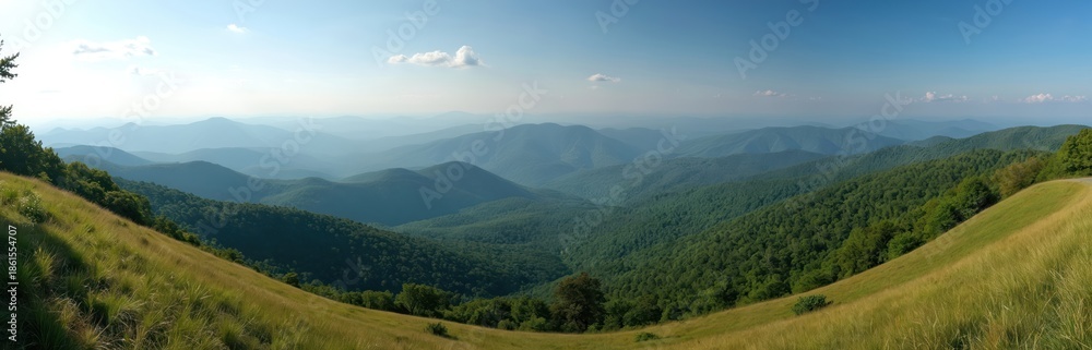 Obraz premium Panoramic view of rolling green mountains under a blue sky. Hazy layers of Appalachian ridges stretch to the horizon from a grassy overlook on the Blue Ridge Parkway.