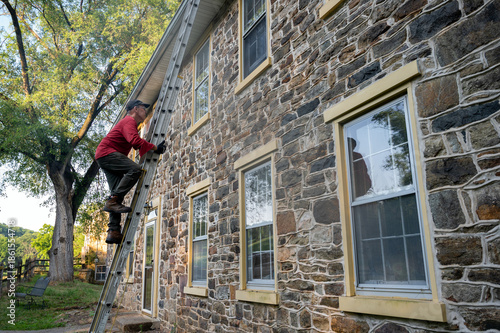 Foto Low angle view of man homeowner climbing dangerous ladder against old stone farm