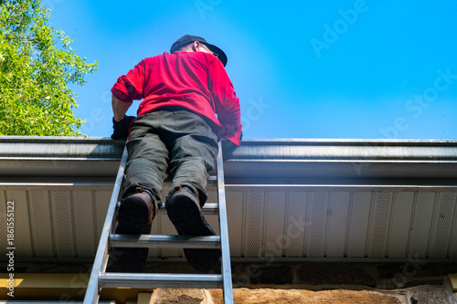 Εκτύπωση καμβά Low angle view of man homeowner climbing dangerous ladder against old stone farm