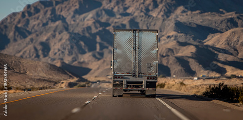 Canvas Print Following behind a silver 18 wheel truck on a two lane highway in the desert with a rocky hill in the distance