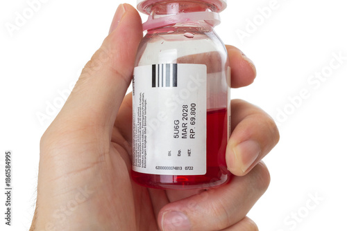 Male hand holding a small transparent plastic bottle of red liquid medicine or syrup. The white label clearly displays the expiration date 