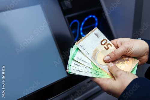 Картината върху платно Hands holding various banknotes in front of an ATM machine, showcasing cash with